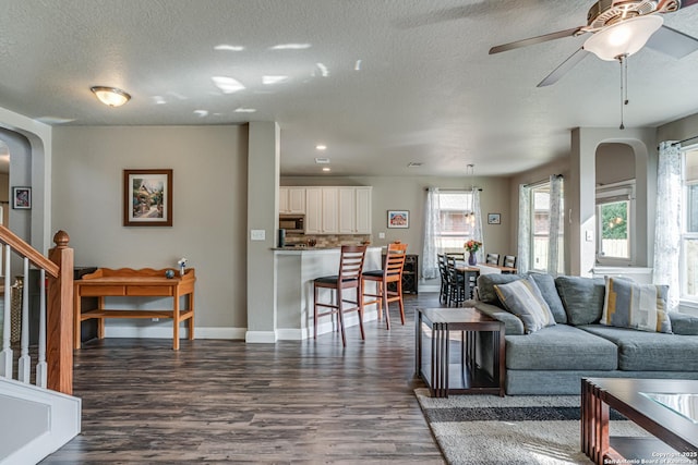 214 Ridge Blf, Cibolo, TX 78108 - living room featuring dark wood-style flooring, a textured ceiling, arched walkways, baseboards, and ceiling fan