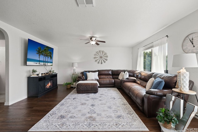184 Jolie Cir, Boerne, TX 78015 - living area featuring arched walkways, dark wood-style flooring, ceiling fan, a fireplace, and a textured ceiling