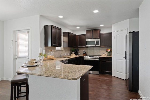 184 Jolie Cir, Boerne, TX 78015 - kitchen with appliances with stainless steel finishes, a peninsula, dark brown cabinets, backsplash, and dark wood-style flooring