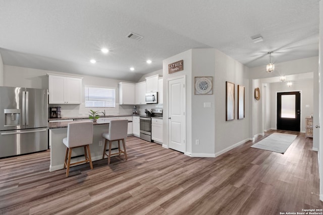 6038 Ballast Trl, New Braunfels, TX 78132 - kitchen with stainless steel appliances, a kitchen island, white cabinets, a breakfast bar, and wood finished floors