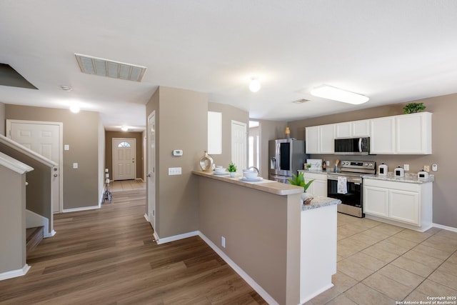 kitchen with stainless steel appliances, white cabinetry, a peninsula, baseboards, and light wood-style floors