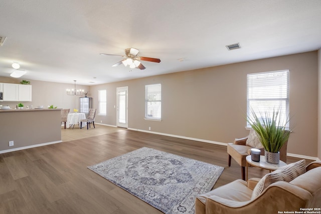 living room with ceiling fan, a chandelier, baseboards, and light wood-type flooring