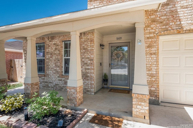 property entrance featuring brick siding, a porch, and an attached garage