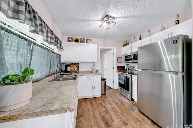 8239 Glen Lark, San Antonio, TX 78239 - kitchen with appliances with stainless steel finishes, a sink, a textured ceiling, light wood finished floors, and tasteful backsplash