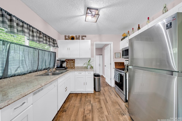 8239 Glen Lark, San Antonio, TX 78239 - kitchen with stainless steel appliances, a sink, wood finished floors, a textured ceiling, and white cabinetry