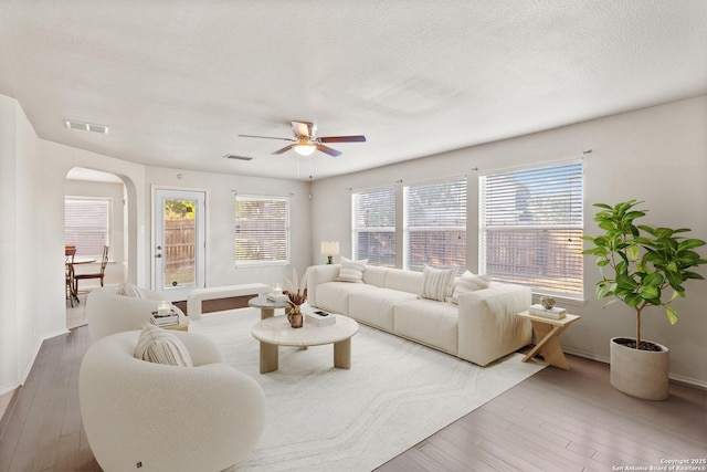 living room featuring arched walkways, a ceiling fan, wood finished floors, and baseboards