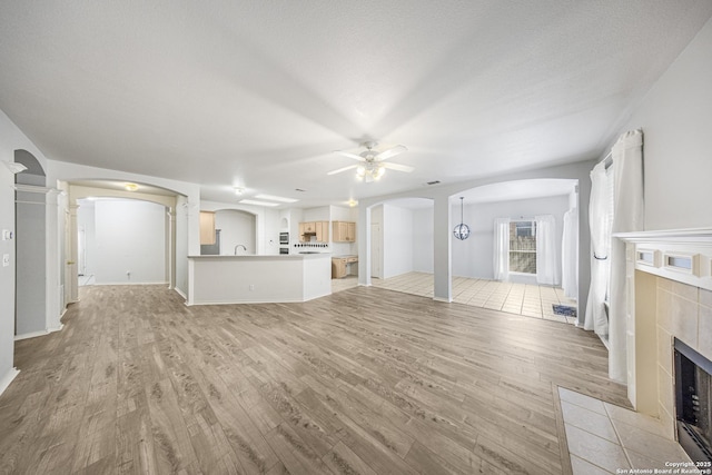 4726 Shavano Bark, San Antonio, TX 78230 - unfurnished living room featuring arched walkways, a tiled fireplace, light wood finished floors, and ceiling fan