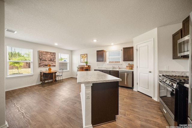 9827 Western Sedge, San Antonio, TX 78254 - kitchen with appliances with stainless steel finishes, dark brown cabinets, light countertops, wood finished floors, and a kitchen island