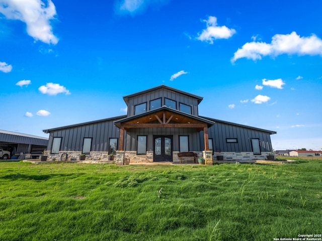back of house with board and batten siding, french doors, a yard, and stone siding