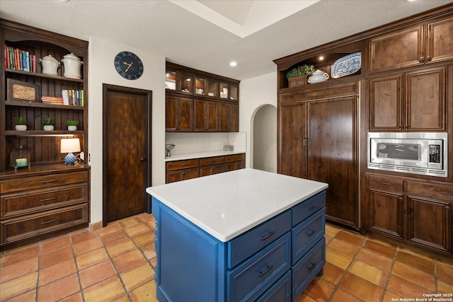8122 Triple Crown, Fair Oaks Ranch, TX 78015 - kitchen featuring stainless steel microwave, open shelves, arched walkways, light countertops, and a center island