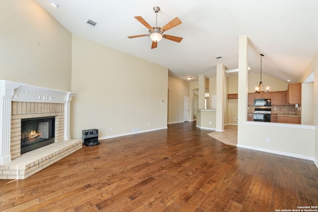 24931 Crescent Run, San Antonio, TX 78258 - unfurnished living room featuring vaulted ceiling, ceiling fan, wood finished floors, a brick fireplace, and a chandelier