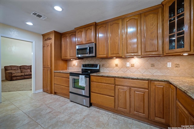 103 River Mdw, Castroville, TX 78009 - kitchen with appliances with stainless steel finishes, brown cabinets, light stone counters, glass insert cabinets, and recessed lighting