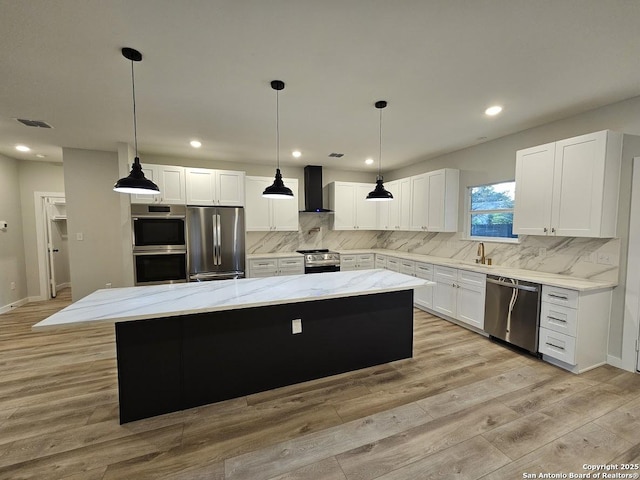 kitchen featuring stainless steel appliances, wall chimney exhaust hood, a center island, light wood-style flooring, and backsplash