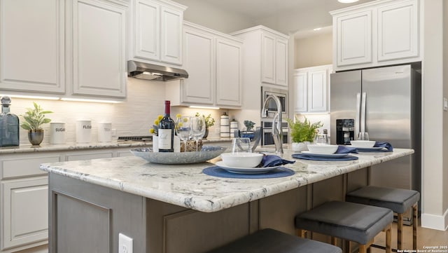 4207 Colina Crst, San Antonio, TX 78261 - kitchen with under cabinet range hood, white cabinets, decorative backsplash, a kitchen island with sink, and a kitchen bar