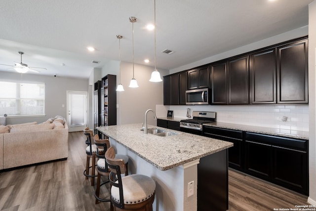 11510 Bakersfield Pass, San Antonio, TX 78245 - kitchen featuring stainless steel appliances, a sink, open floor plan, dark wood-style floors, and a center island with sink