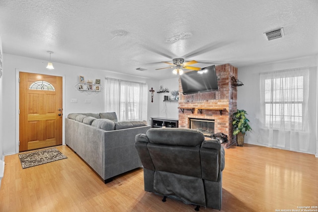 1130 Stone Gdn, New Braunfels, TX 78130 - living area featuring a textured ceiling, light wood-type flooring, ceiling fan, and a brick fireplace