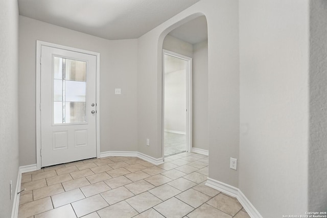 foyer with arched walkways, light tile patterned floors, and baseboards