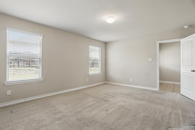 spare room featuring light carpet, baseboards, a textured ceiling, and a smoke detector