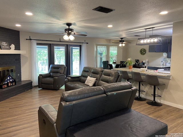 326 Riverview, Mcqueeney, TX 78123 - living room with a ceiling fan, wood finished floors, a textured ceiling, baseboards, and a brick fireplace