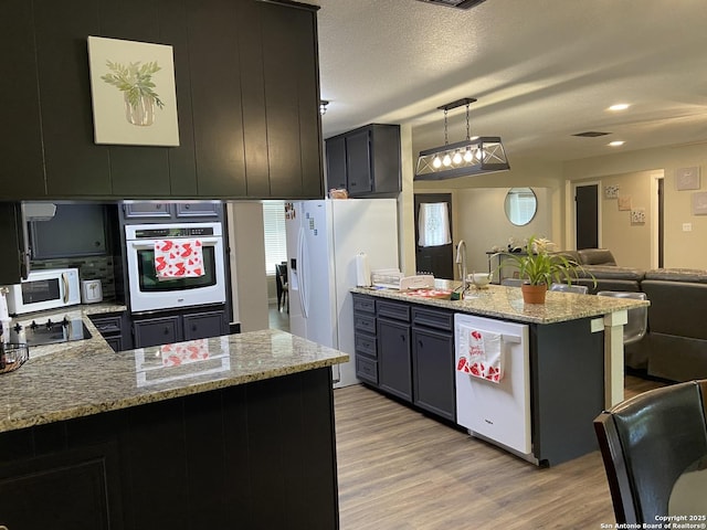 326 Riverview, Mcqueeney, TX 78123 - kitchen featuring white appliances, a peninsula, light wood-style floors, open floor plan, and light stone counters