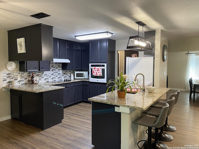 326 Riverview, Mcqueeney, TX 78123 - kitchen with white appliances, a peninsula, decorative backsplash, a breakfast bar, and under cabinet range hood