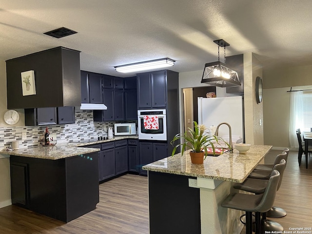 326 Riverview, Mcqueeney, TX 78123 - kitchen featuring white appliances, tasteful backsplash, a kitchen breakfast bar, light stone countertops, and a textured ceiling