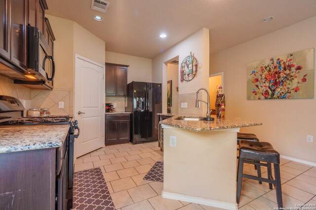 11607 Pelican Pass, San Antonio, TX 78221 - kitchen with range with gas stovetop, black refrigerator with ice dispenser, a sink, a peninsula, and a breakfast bar area