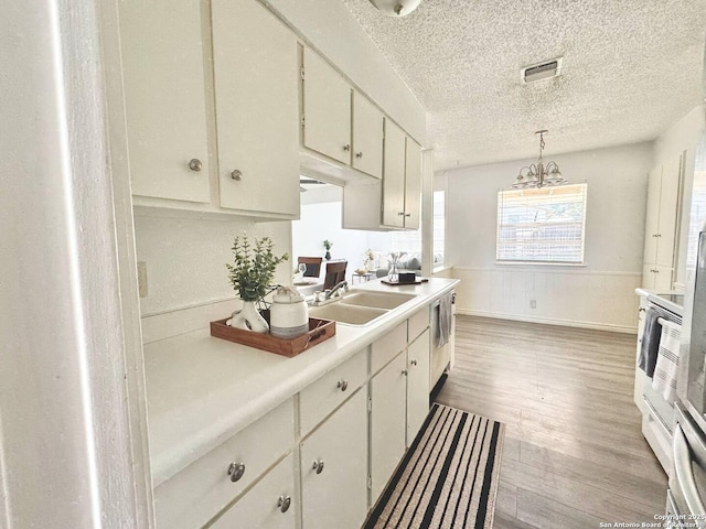 1303 Billings Dr, San Antonio, TX 78245 - kitchen with a sink, a textured ceiling, light countertops, wood finished floors, and white cabinetry