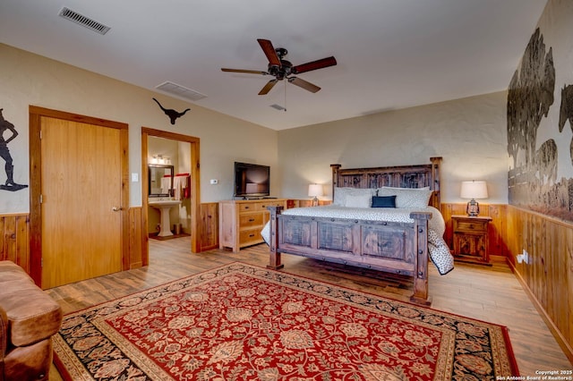 24005 Pedernales Canyon Trl, Spicewood, TX 78669 - bedroom with light wood finished floors, wooden walls, a wainscoted wall, connected bathroom, and a ceiling fan