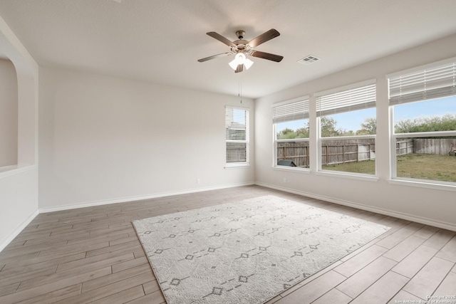 unfurnished room featuring a ceiling fan, light wood-style flooring, arched walkways, and baseboards