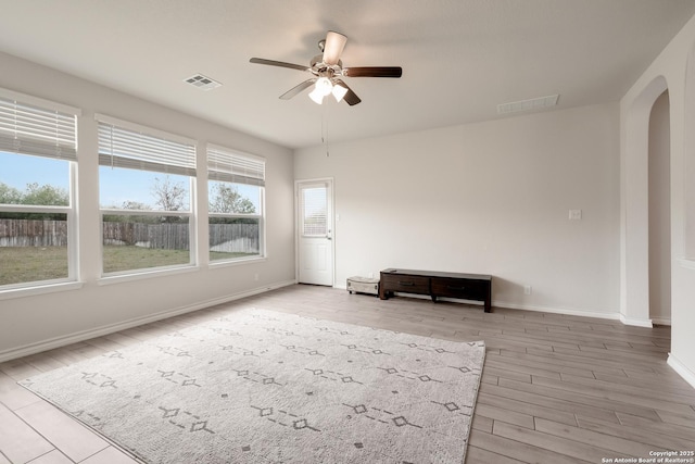 empty room featuring arched walkways, a ceiling fan, wood finished floors, and baseboards