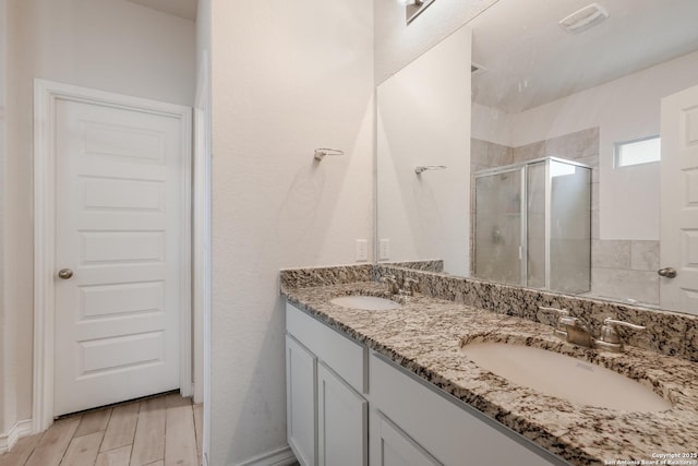 bathroom featuring a shower stall, double vanity, and wood finished floors
