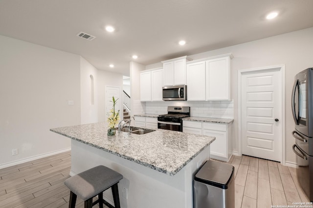 kitchen with stainless steel appliances, a sink, wood finish floors, a breakfast bar, and backsplash