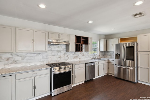 kitchen with appliances with stainless steel finishes, under cabinet range hood, a sink, dark wood finished floors, and tasteful backsplash