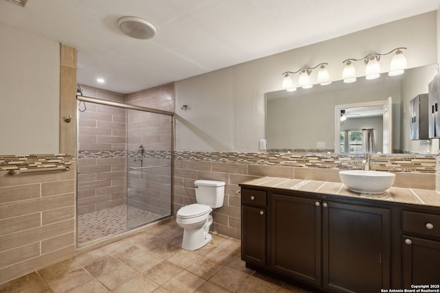 full bathroom featuring tile walls, a shower stall, toilet, a ceiling fan, and vanity