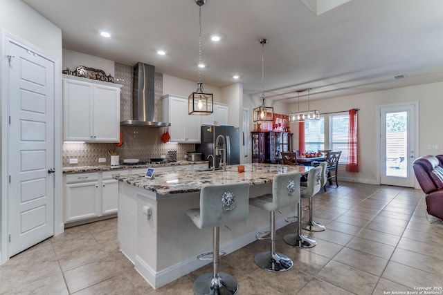29121 Ismorada, San Antonio, TX 78260 - kitchen featuring wall chimney range hood, black fridge with ice dispenser, a center island with sink, backsplash, and a kitchen bar