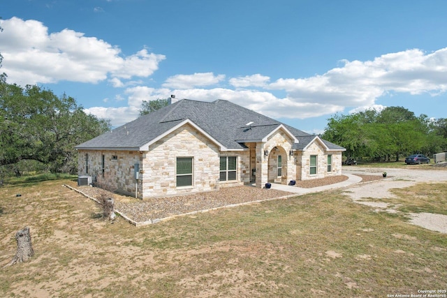 346 Broken Arrow, Floresville, TX 78114 - french provincial home featuring stone siding, roof with shingles, central air condition unit, and a front lawn