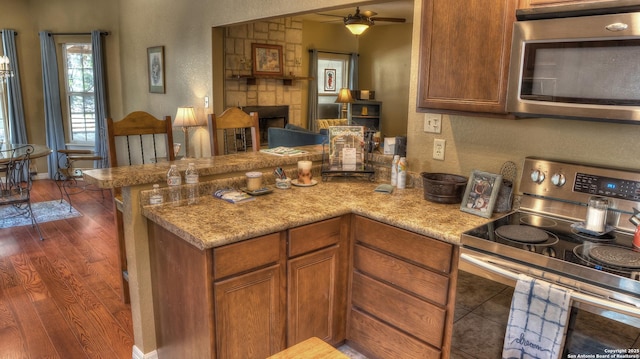 211 Roy Chisum Rd, Leakey, TX 78873 - kitchen with appliances with stainless steel finishes, a peninsula, wood finished floors, brown cabinets, and a ceiling fan