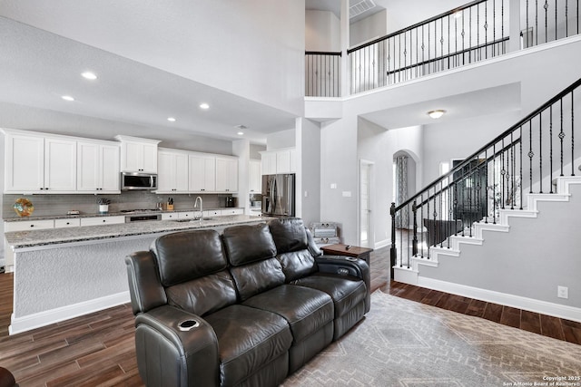 27210 Camellia, Boerne, TX 78015 - living room featuring dark wood-type flooring, baseboards, arched walkways, a towering ceiling, and stairs