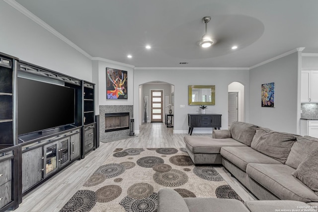 living area featuring arched walkways, crown molding, light wood-style floors, a fireplace, and recessed lighting