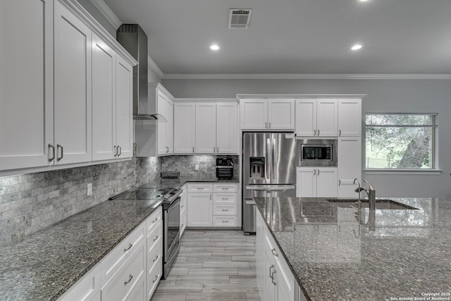kitchen with stainless steel appliances, a sink, wall chimney exhaust hood, crown molding, and white cabinetry