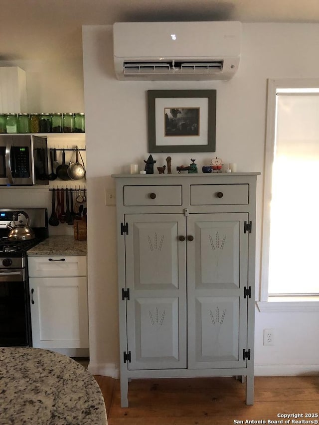 345 Westminster, San Antonio, TX 78228 - detailed view of stainless steel appliances, a wall mounted air conditioner, white cabinetry, light stone counters, and wood finished floors