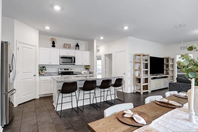 7910 Asp Pt, San Antonio, TX 78253 - kitchen featuring appliances with stainless steel finishes, white cabinetry, a center island with sink, light stone countertops, and a breakfast bar