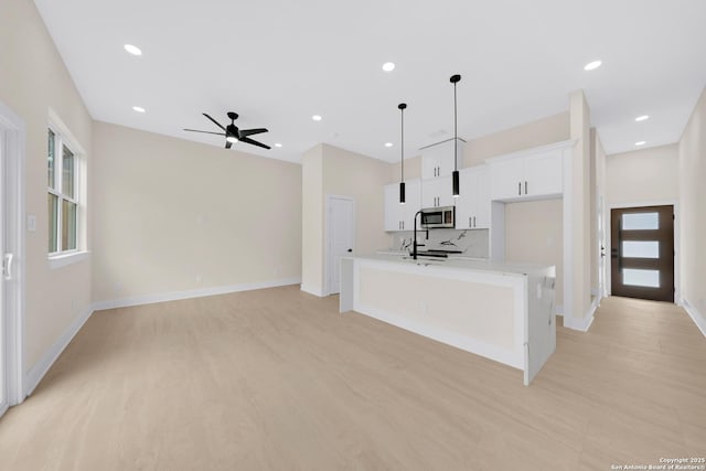 kitchen with stainless steel microwave, an island with sink, white cabinets, a ceiling fan, and light countertops