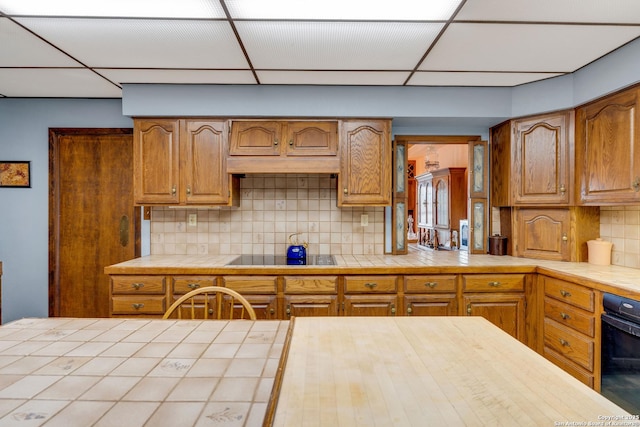 3619 Running Spgs, San Antonio, TX 78261 - kitchen featuring tile countertops, black electric stovetop, tasteful backsplash, a drop ceiling, and brown cabinetry