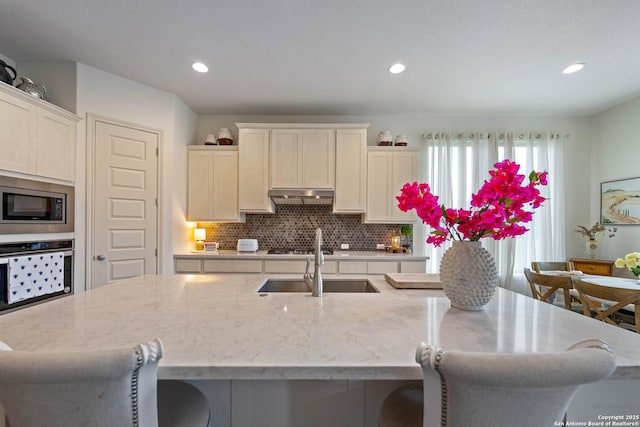 1235 Yaupon, New Braunfels, TX 78132 - kitchen featuring stainless steel appliances, a sink, under cabinet range hood, a kitchen bar, and decorative backsplash