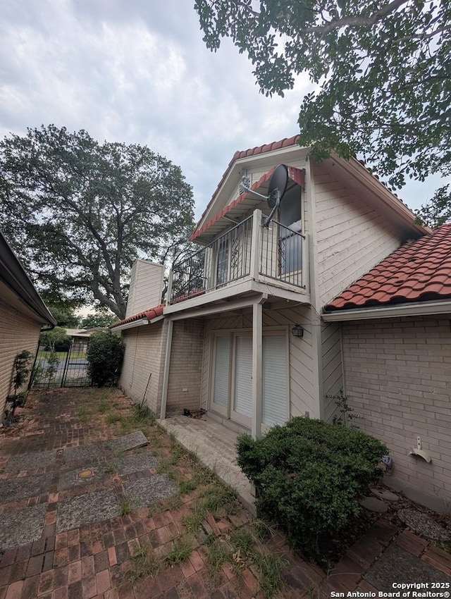 6410 Firestone, San Antonio, TX 78244 - view of property exterior featuring a balcony, a tile roof, brick siding, and fence