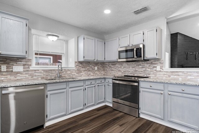 6909 Quail Lk, San Antonio, TX 78244 - kitchen featuring stainless steel appliances, a sink, a textured ceiling, dark wood-style flooring, and tasteful backsplash