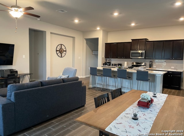 kitchen featuring stainless steel microwave, range, light countertops, a center island with sink, and open floor plan
