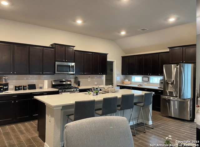 kitchen with stainless steel appliances, an island with sink, tasteful backsplash, wood finish floors, and recessed lighting